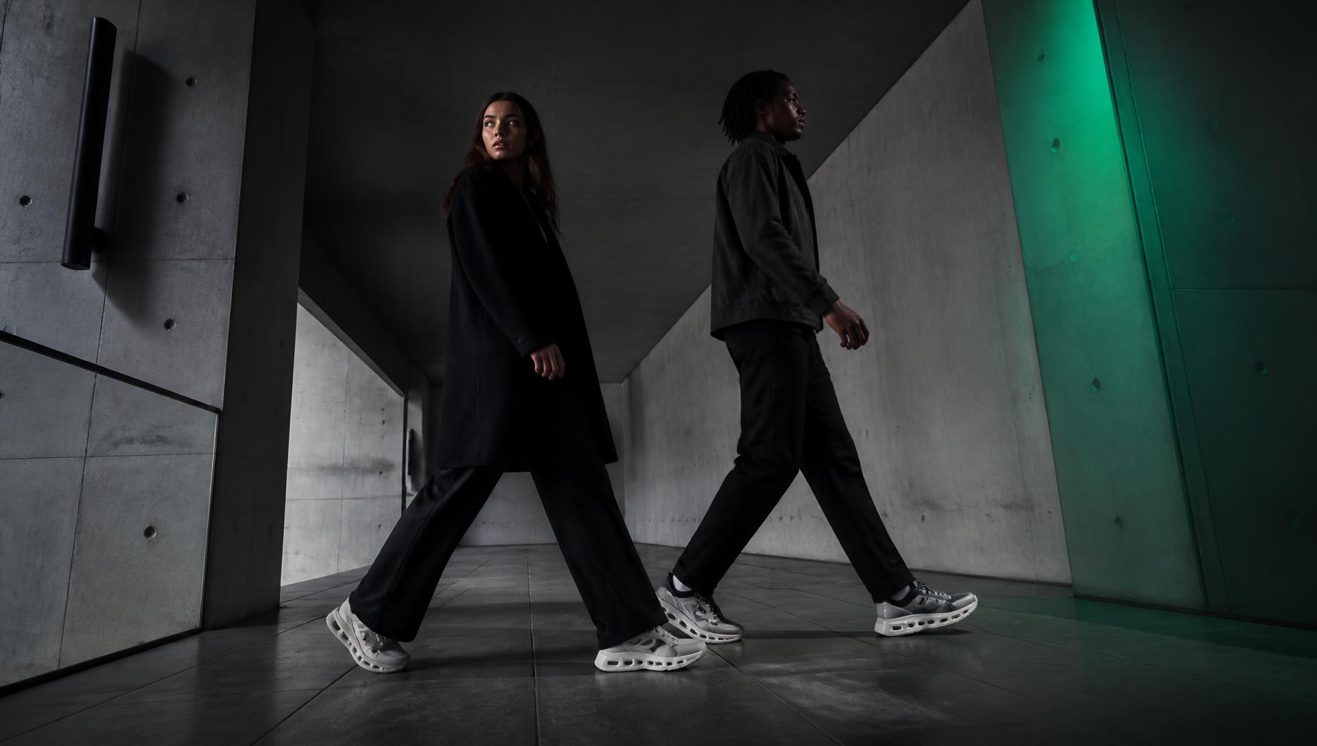 Two people walking in a concrete corridor lit with a green accent